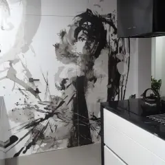 Nowoczesna kuchnia z czarnym blatem i białymi szafkami. Na ścianie artystyczny mural, który świetnie maskuje drzwi.