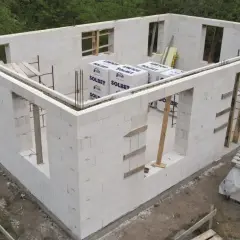 Budowa domu z bloczków z betonu komórkowego. Widoczne ściany z otworami okiennymi i drzwiowymi, materiały budowlane.