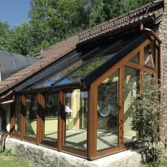 Nowoczesny ogród zimowy na tarasie, z drewnianymi ramami i przeszklonym dachem, idealny do relaksu przez cały rok.