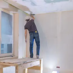 Pracownik szpachluje łączenia płyt gipsowych na suficie. Sprawdź, jaka jest szpachlowanie łączeń płyt gipsowych cena.