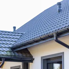 Szary dach z dachówki ceramicznej, rynny i komin. Sprawdź, jaka jest dachówka ceramiczna cena za m2.