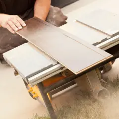 Ręce układają panel winylowy na pile stołowej, pokazując, czym ciąć panele winylowe.