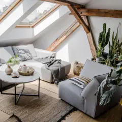 Przytulny salon z szarą kanapą, narzutą, poduszkami i roślinami. Dodatki tworzą ciepłą atmosferę.