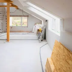 Wnętrze w trakcie rozbudowy domu. Widoczne rusztowania, materiały budowlane, instalacje elektryczne i okna.