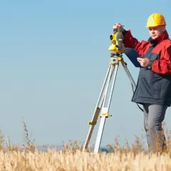 Geodeta w żółtym kasku pracuje z tachimetrem w polu. Zastanawiasz się, ile kosztuje geodeta?