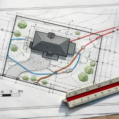 Projekt zagospodarowania terenu z domem, drzewami i zaznaczonymi instalacjami. Linijka geodezyjna obok.