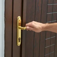Dłoń naciska na złoty uchwyt drzwi, sugerując, jak otworzyć drzwi bez klucza, gdy zamek jest odblokowany.