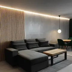 Nowoczesny salon w stylu loft z drewnianą ścianką, szarą sofą i jadalnią.