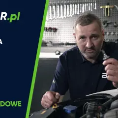 Mężczyzna pokazuje, jak wymienić żarówkę samochodową. W tle warsztat z narzędziami.