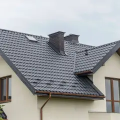Nowoczesne opierzenie dachu z ciemnej blachodachówki, z dwoma kominami i okapem.