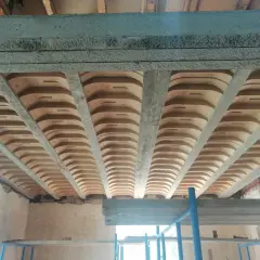 Widok od dołu na betonowe belki stropowe i pustaki ceramiczne, tworzące przestrzeń przypominającą sufit katedralny.