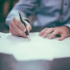 Dłoń pisze na papierze, być może notując, jak wygląda numer księgi wieczystej.