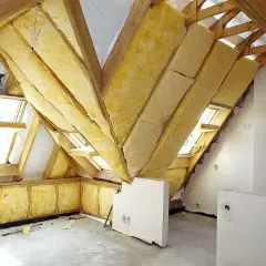 Trwa adaptacja poddasza. Widoczne są drewniane konstrukcje dachu, okna dachowe oraz żółta wełna mineralna jako izolacja.
