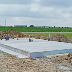 Solidny fundament z betonu, gotowy na budowę domu. Wokół piasek i zielone pola.