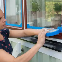 Kobieta okleja taśmą malarską drewniane okno, przygotowując je do malowania.