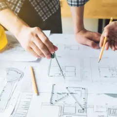 Rysowanie szczegółów projektu budowlanego. Inżynierowie analizują plany, używając cyrkla i ołówka.