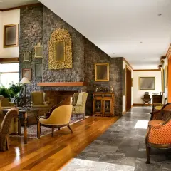Elegancki salon w stylu kolonialnym, z kamiennym kominkiem, drewnianą podłogą i bogato zdobionymi meblami.