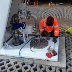 Pracownik w pomarańczowej kamizelce serwisuje instalację przy studni głębinowej.