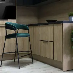 Nowoczesny blat z hokerami w kuchni. Drewniane fronty szafek i zielony, aksamitny hoker tworzą stylowe wnętrze.
