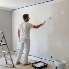Mężczyzna maluje ścianę na biało. Ciekawi go, ile schnie grunt, zanim nałoży kolejną warstwę.