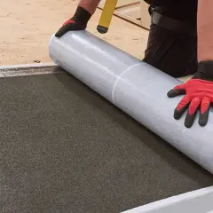 Ręce w rękawiczkach rozwijają papę podkładową na dachu.