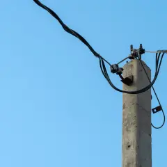 Stary słup na działce ponad 30 lat, z kablami elektrycznymi na tle błękitnego nieba.