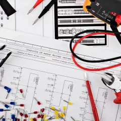 Narzędzia i schematy do elektryki w domu: kombinerki, multimetr i okablowanie na tle planów instalacji.