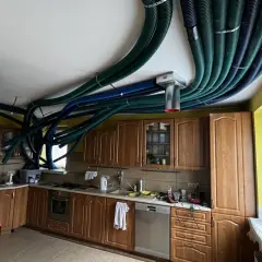 Instalacja rekuperacji w starym domu. W kuchni na suficie widać gęsto ułożone, zielone i niebieskie przewody wentylacyjne.
