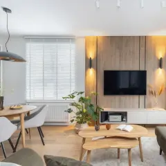 Przytulny salon inspiracje: drewniana ściana z TV, jadalnia, rośliny i wygodna sofa tworzą ciepłą atmosferę.
