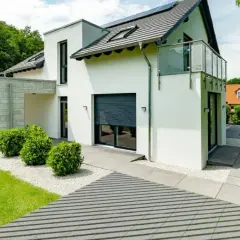 Nowoczesna biała elewacja wokół drzwi wejściowych, z betonowym zadaszeniem i zielenią.