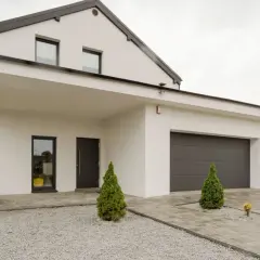 Nowoczesny dom z garażem i zadaszeniem. Podjazd z kostki brukowej i żwiru to świetny pomysł na tani podjazd.