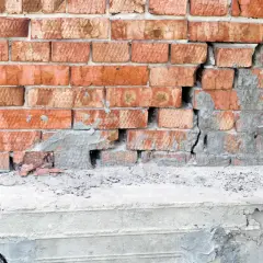 Uszkodzona ceglana ściana z widocznym pęknięciem w betonie, wskazującym na podbijanie fundamentów.