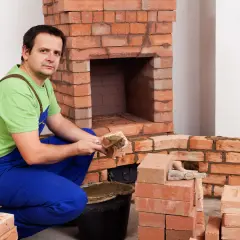 Murarz układa cegły szamotowe, budując kominek.
