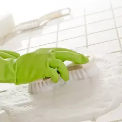 Ręka w zielonej rękawiczce szoruje szczotką białe fugi pokryte pianą.