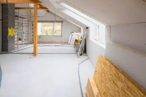 Wnętrze w trakcie rozbudowy domu. Widoczne rusztowania, materiały budowlane, instalacje elektryczne i okna.