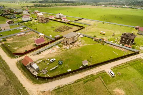Działka z domami w budowie i gotowymi, otoczona płotem. Widać drogi dojazdowe, co sugeruje służebność drogi problemy.