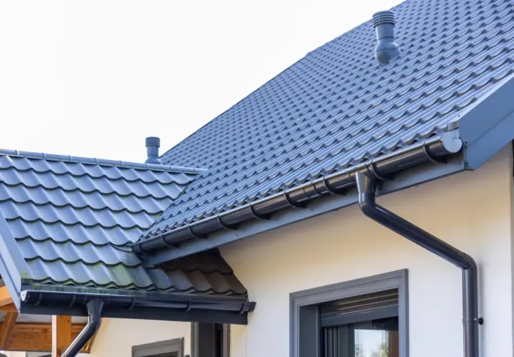 Szary dach z dachówki ceramicznej, rynny i komin. Sprawdź, jaka jest dachówka ceramiczna cena za m2.