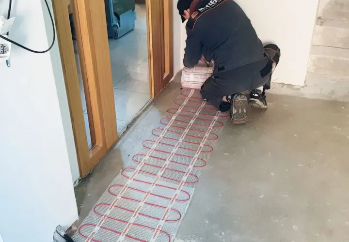 Instalator montuje matę grzewczą, przygotowując podłogę do komfortowego ogrzewania. To inwestycja w przyszłość, która obniży koszt ogrzewania podłogowego.