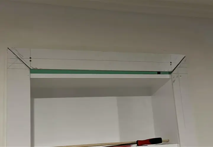 Montaż ukrytych drzwi w regale. Widoczne elementy konstrukcyjne i narzędzia.