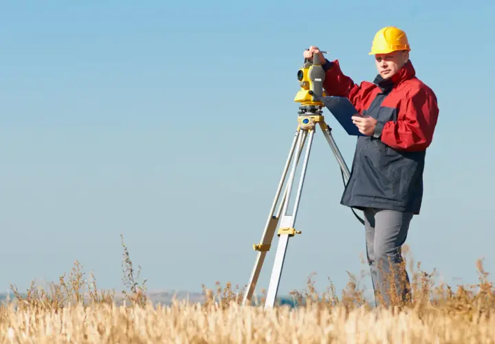 Geodeta w żółtym kasku pracuje z tachimetrem w polu. Zastanawiasz się, ile kosztuje geodeta?