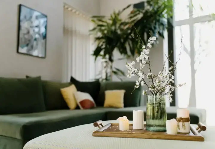 Zielona kanapa, świece i kwitnące gałązki tworzą harmonię w salonie, zgodną z zasadami feng shui.