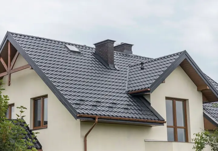 Nowoczesne opierzenie dachu z ciemnej blachodachówki, z dwoma kominami i okapem.
