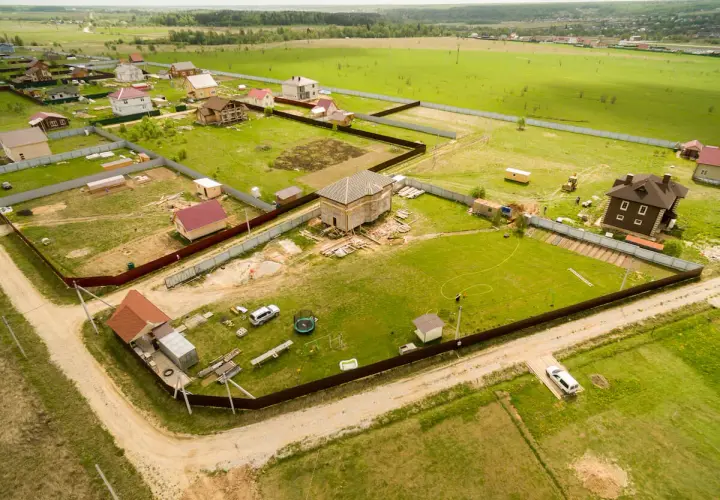 Działka z domami w budowie i gotowymi, otoczona płotem. Widać drogi dojazdowe, co sugeruje służebność drogi problemy.