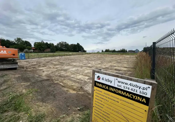 Tablica informacyjna budowy placu pod dom jednorodzinny. Widoczny koparka i niebieska toaleta.