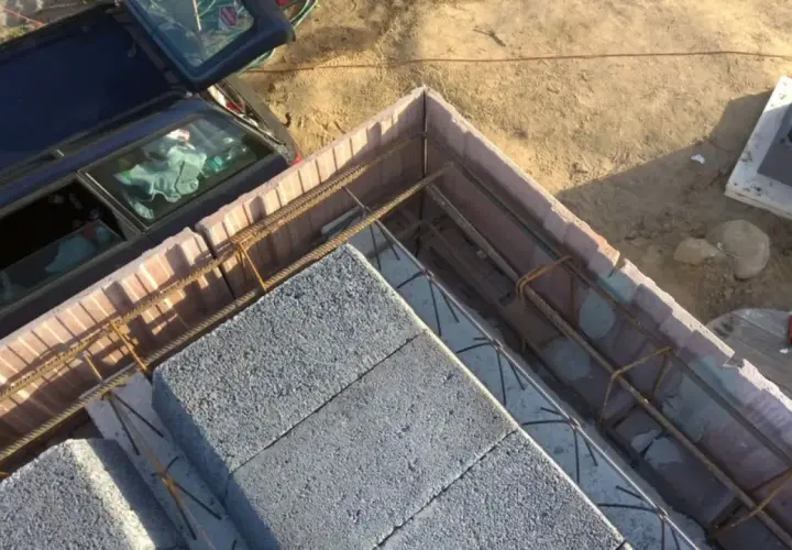 Szalowanie stropu z bloczków betonowych i zbrojenia. Obok stoi samochód.