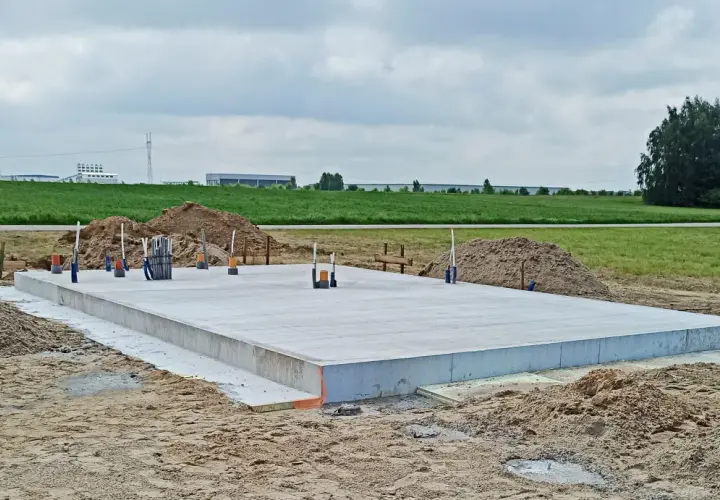 Solidny fundament z betonu, gotowy na budowę domu. Wokół piasek i zielone pola.