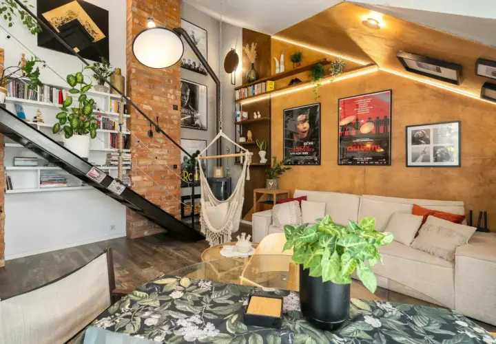 Salon w stylu loftowym z ceglaną ścianą, metalowymi schodami, wiszącym fotelem i wygodną kanapą.