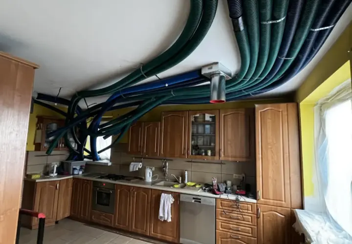 Instalacja rekuperacji w starym domu. W kuchni na suficie widać gęsto ułożone, zielone i niebieskie przewody wentylacyjne.