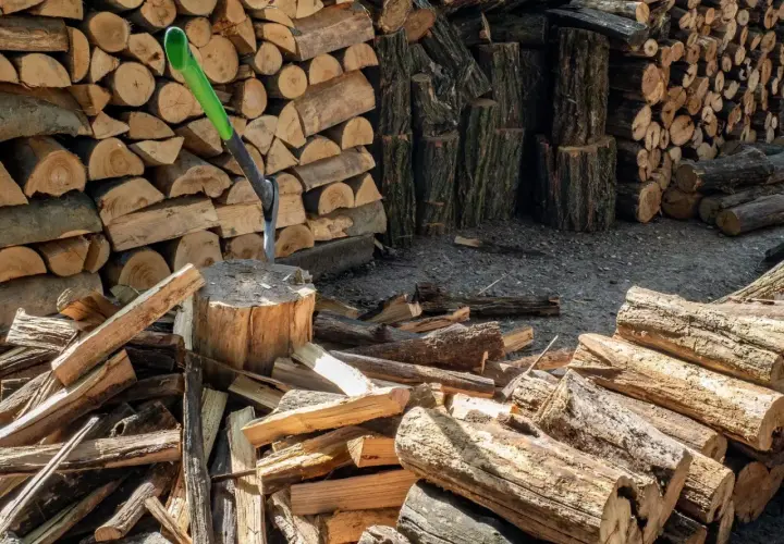 Stos drewna opałowego, siekiera wbita w pień. Wiele polan, przygotowanie do zimy. Cena drewna opałowego może być wysoka.