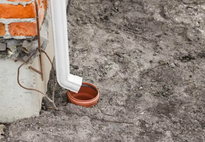 Biała rura spustowa odprowadza wodę z rynien do gruntu, do ceramicznej studzienki.